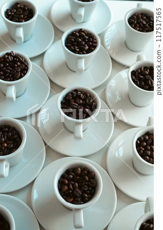 White coffee cups and saucers with coffee beans arranged on a table, vertical White coffee cups and saucers with coffee beans arranged on a table, vertical 117517565