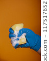 Hand in blue rubber glove holding soap sponge on orange background 117517652
