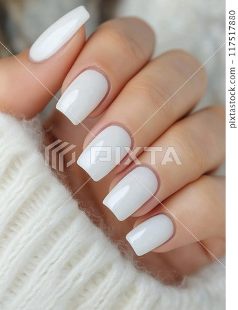 Elegant white manicure with shiny finish on cozy knitted sweater background 117517880