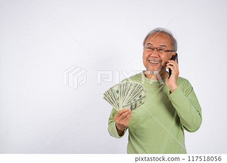 Portrait Asian smiling old man is holding a bunch of money fan and talking on cell mobile phone studio shot isolated on white background. happy elderly hold dollar banknotes Portrait Asian smiling old man is holding a bunch of money fan and talking on cell mobile phone studio shot isolated on white background. happy elderly hold dollar banknotes 117518056
