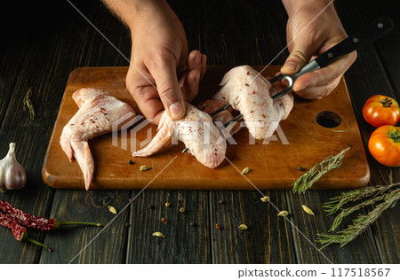 The chef threads chicken wings on a fork. The concept of business service in a restaurant or hotel. Cooking Buffalo wings on the kitchen table The chef threads chicken wings on a fork. The concept of business service in a restaurant or hotel. Cooking Buffalo wings on the kitchen table 117518567