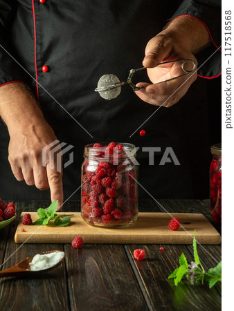 Chef preserves red raspberry in a jar. Concept of cooking sweet jam with sugar on the kitchen table. Adding citric acid to raspberries Chef preserves red raspberry in a jar. Concept of cooking sweet jam with sugar on the kitchen table. Adding citric acid to raspberries 117518568