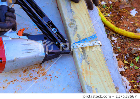 Nail wooden beams to concrete with an air pneumatic hammer during new home construction 117518667