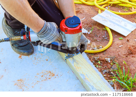 Nailing wooden beams to concrete with an air pneumatic hammer during new house construction framing 117518668