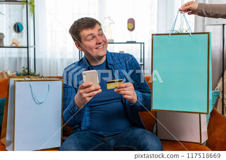 Happy shopaholic consumer man making online order payment with credit card receive shopping bags 117518669