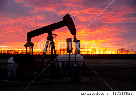 Striking orange and purple sunrise in prairies and the silhouette of an oil pump extracting fuel. 117518928