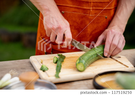 Close up of man holding sharp knife, peeling cucumber. Preparing vegetables for an outdoor barbecue. Close up of man holding sharp knife, peeling cucumber. Preparing vegetables for an outdoor barbecue. 117519250