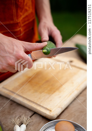 Close up of man holding sharp knife, peeling cucumber. Preparing vegetables for an outdoor barbecue. Close up of man holding sharp knife, peeling cucumber. Preparing vegetables for an outdoor barbecue. 117519251