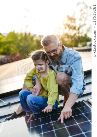 Dad and girl on roof with solar panels, learning about solar energy. Rooftop solar or photovoltaic system. Sustainable future for next generation. 117519261