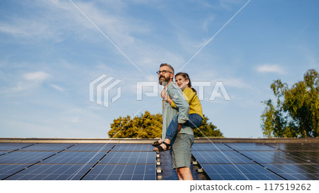 Father with girl on roof with solar panels, piggyback ride. Rooftop solar or photovoltaic system. Sustainable future for next generation. 117519262