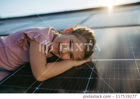 Cute girl lying on solar panels roof, shot with copy space. Rooftop solar or photovoltaic system. Sustainable future for next generation. Cute girl lying on solar panels roof, shot with copy space. Rooftop solar or photovoltaic system. Sustainable future for next generation. 117519277