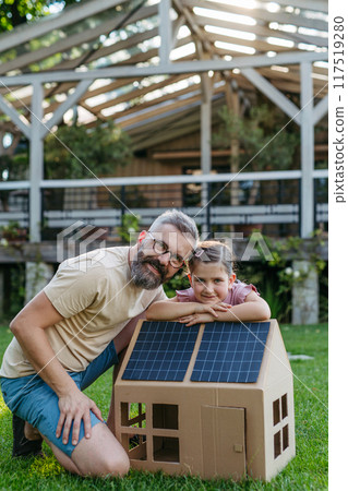 Dad and girl plying with house with solar panels on roof, learning about solar energy. Rooftop solar or photovoltaic system. Sustainable future for next generation. 117519280