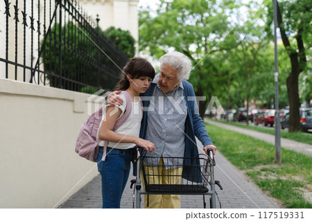 Grandma picking up girl after first day of school. Granddaughter spending time with senior grandmother outdoors in city. 117519331