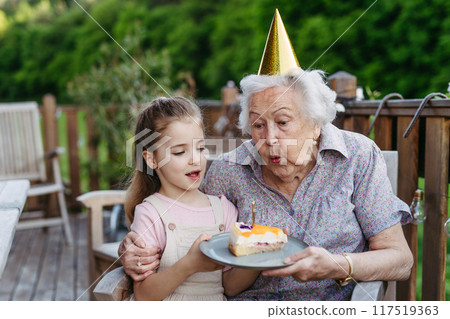 Granddaughter celebrating birthday with elderly grandma, blowing candle on cake. Senior lady spending time with young girl, enjoying together time. Granddaughter celebrating birthday with elderly grandma, blowing candle on cake. Senior lady spending time with young girl, enjoying together time. 117519363