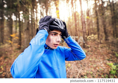 Man putting on helmet before ride on bike in the middle of forest, early autumn morning. Concept of healthy lifestyle. Man putting on helmet before ride on bike in the middle of forest, early autumn morning. Concept of healthy lifestyle. 117519431