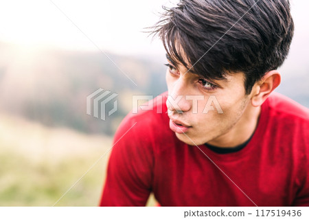 Male runner resting after jog in nature on dirt running trail, enjoying view. Morning running training for young man. Male runner resting after jog in nature on dirt running trail, enjoying view. Morning running training for young man. 117519436