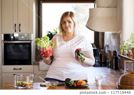 Overweight woman in the kitchen, making homemade lunch. Choosing healthy food, making and eating vegetable salad. Overweight woman in the kitchen, making homemade lunch. Choosing healthy food, making and eating vegetable salad. 117519446
