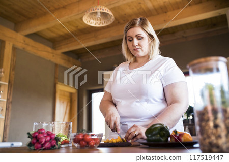 Overweight woman in the kitchen, making homemade lunch. Choosing healthy food, making and eating vegetable salad. Overweight woman in the kitchen, making homemade lunch. Choosing healthy food, making and eating vegetable salad. 117519447