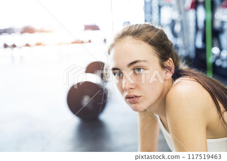 Young fitness girl with dental braces feeling exhausted after hard workout in gym, holding knees, breathing. 117519463