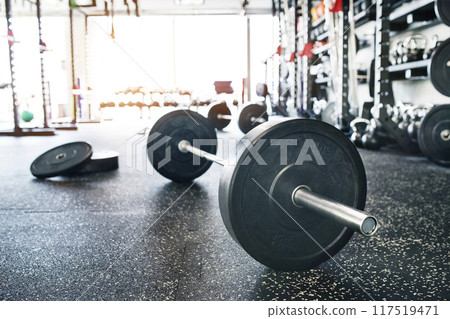 Rows of metal barbells on floor and rack for strength training in gym. 117519471