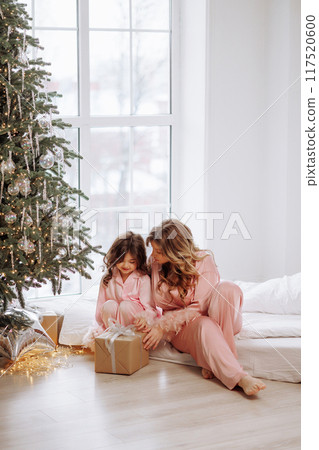 A woman and a child are sitting on a bed in front of a Christmas tree A woman and a child are sitting on a bed in front of a Christmas tree 117520600