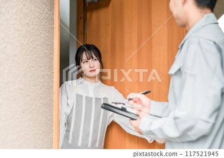 A housewife looks annoyed at a man in work clothes who has come to visit her at the entrance 117521945