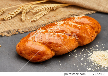 Freshly baked braided bread with sesame seeds on rustic background, ideal for bakery food projects Freshly baked braided bread with sesame seeds on rustic background, ideal for bakery food projects 117522435