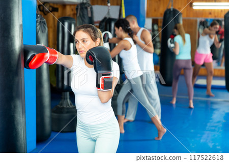 Young hispanic woman in boxing gloves practicing punches on punchbag Young hispanic woman in boxing gloves practicing punches on punchbag 117522618