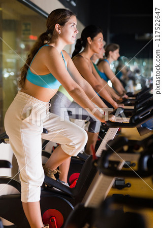 Woman taking indoor cycling class at gym 117522647