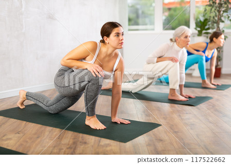 Girl doing Anjaneyasana pose during group yoga workout 117522662