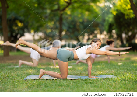 Girl performing balancing table asana during group yoga in park 117522721
