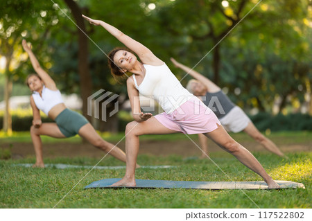Woman performing Utthita Parsvakonasana at group yoga session in park Woman performing Utthita Parsvakonasana at group yoga session in park 117522802