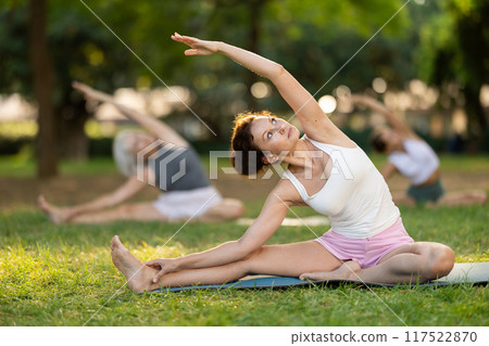 Woman participating in outdoor yoga session in summer park 117522870