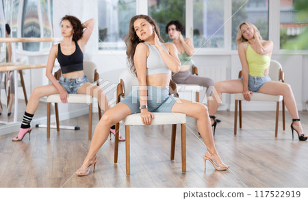 Group of women in high heels rehearsing dance while sitting on chair Group of women in high heels rehearsing dance while sitting on chair 117522919