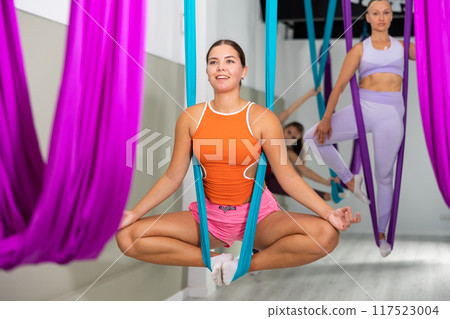 Smiling girl doing bound angle pose in hanging hammock with hands in mudra 117523004