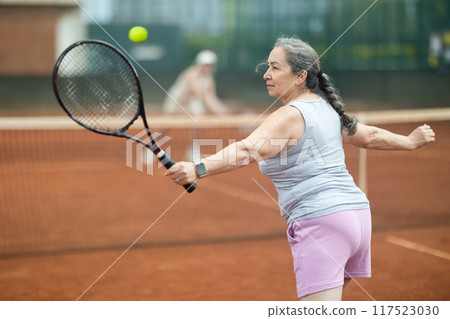 Aged woman playing friendly tennis match outdoors 117523030