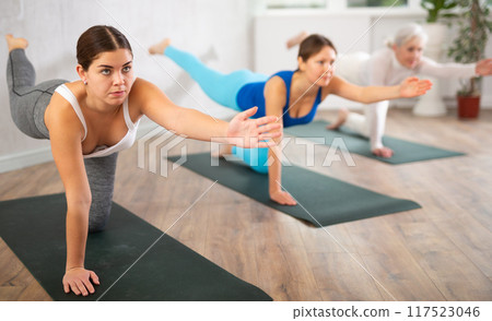 Diligent women practicing balancing table pose of yoga in light fitness room 117523046