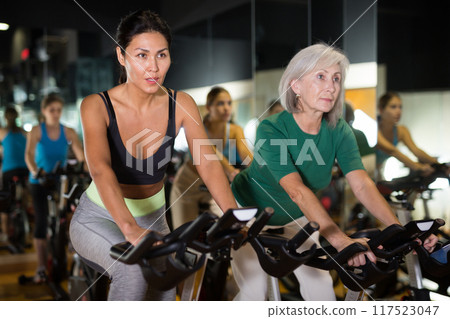 Women training on exercise bikes at gym 117523047