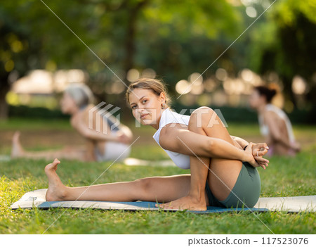 Smiling girl performing seated asana Marichyasana during yoga class in park 117523076