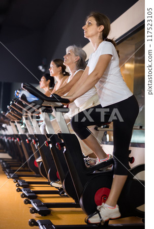 Woman riding stationary bike at fitness center 117523105