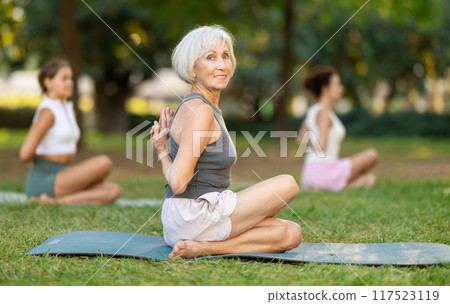 Elderly woman performing Reverse Prayer Gomukhasana during group yoga in park Elderly woman performing Reverse Prayer Gomukhasana during group yoga in park 117523119