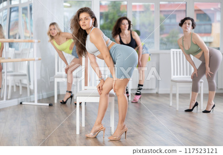 Group of women in high heels rehearsing dance while standing near chair Group of women in high heels rehearsing dance while standing near chair 117523121