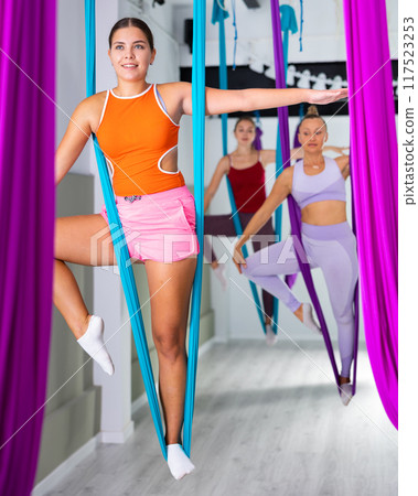 Young girl doing exercises with suspended hammock in aerial yoga studio 117523253