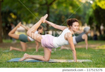 Positive sporty skilled young female teacher demonstrating table pose of yoga in green park at daytime 117523276