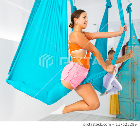 Fit pretty women doing fly yoga stretching exercises in fitness training white gym loft classroom 117523289