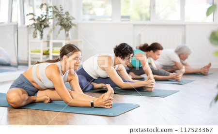 Young girl stretching in Janu Sirsasana during group yoga practice 117523367