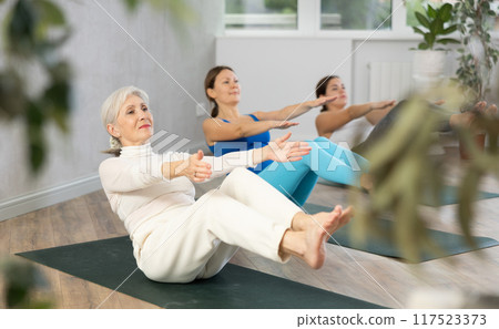 Elderly woman doing Havasana pose during group yoga session Elderly woman doing Havasana pose during group yoga session 117523373
