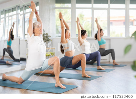 Elderly woman performing Lunge Equestrian Pose in yoga studio Elderly woman performing Lunge Equestrian Pose in yoga studio 117523400
