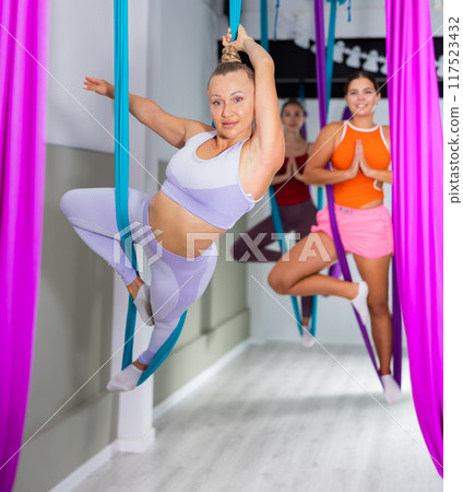 Fit woman enjoying aerial yoga group workout with suspended hammock Fit woman enjoying aerial yoga group workout with suspended hammock 117523432