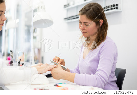 Woman manicurist filing and shaping nails of female client 117523472